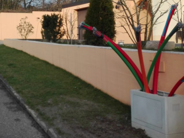 Rode en groene buizen steken uit een betonnen bak naast een grasstrook en een muur