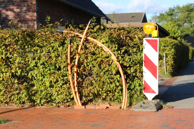 Twee oranje buizen steken uit de grond bij een haag, naast een werfbaken