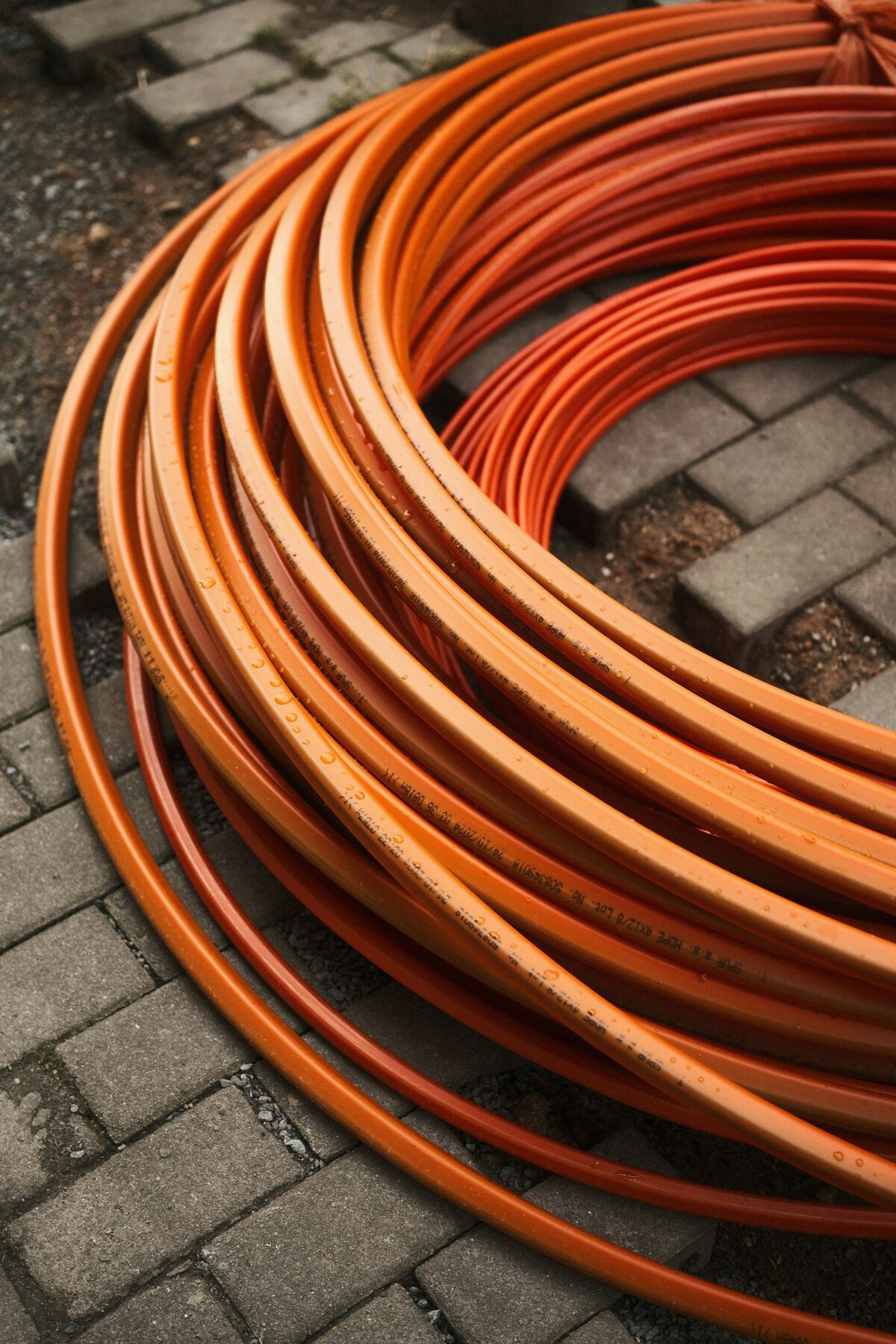 Opgerolde oranje buizen liggen op een voetpad van grijze klinkers